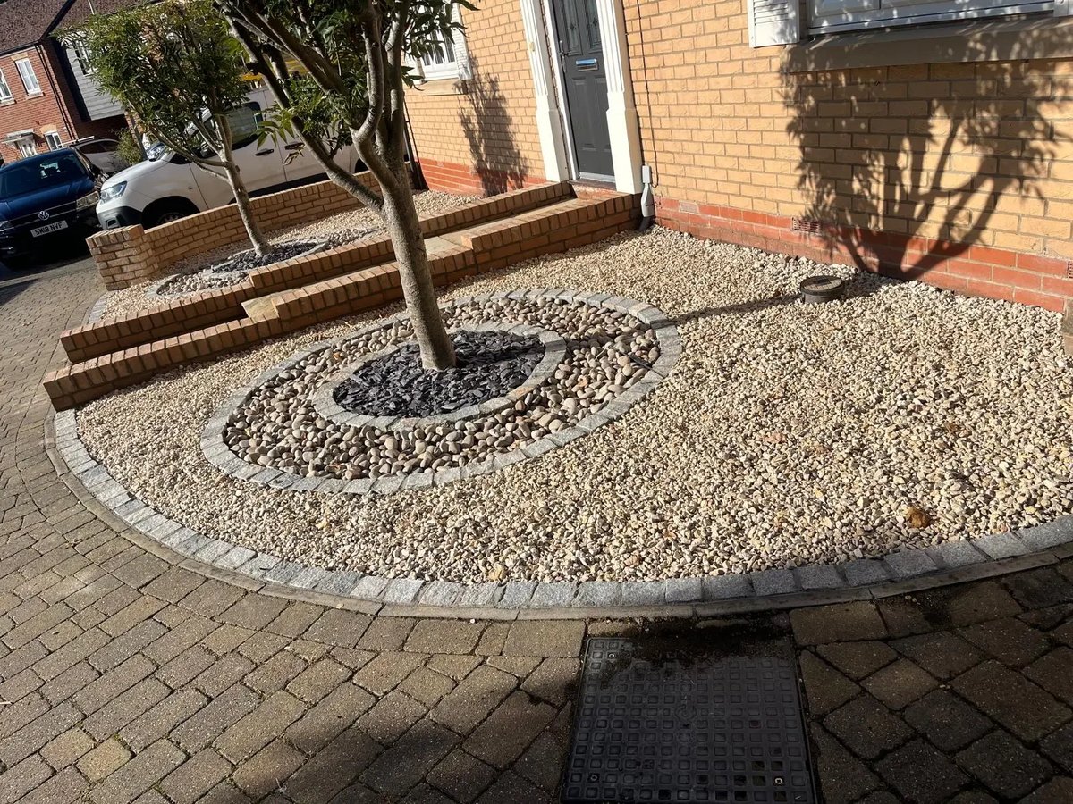 Detailed view of a landscaped gravel front garden with circular stone edging around a mature tree