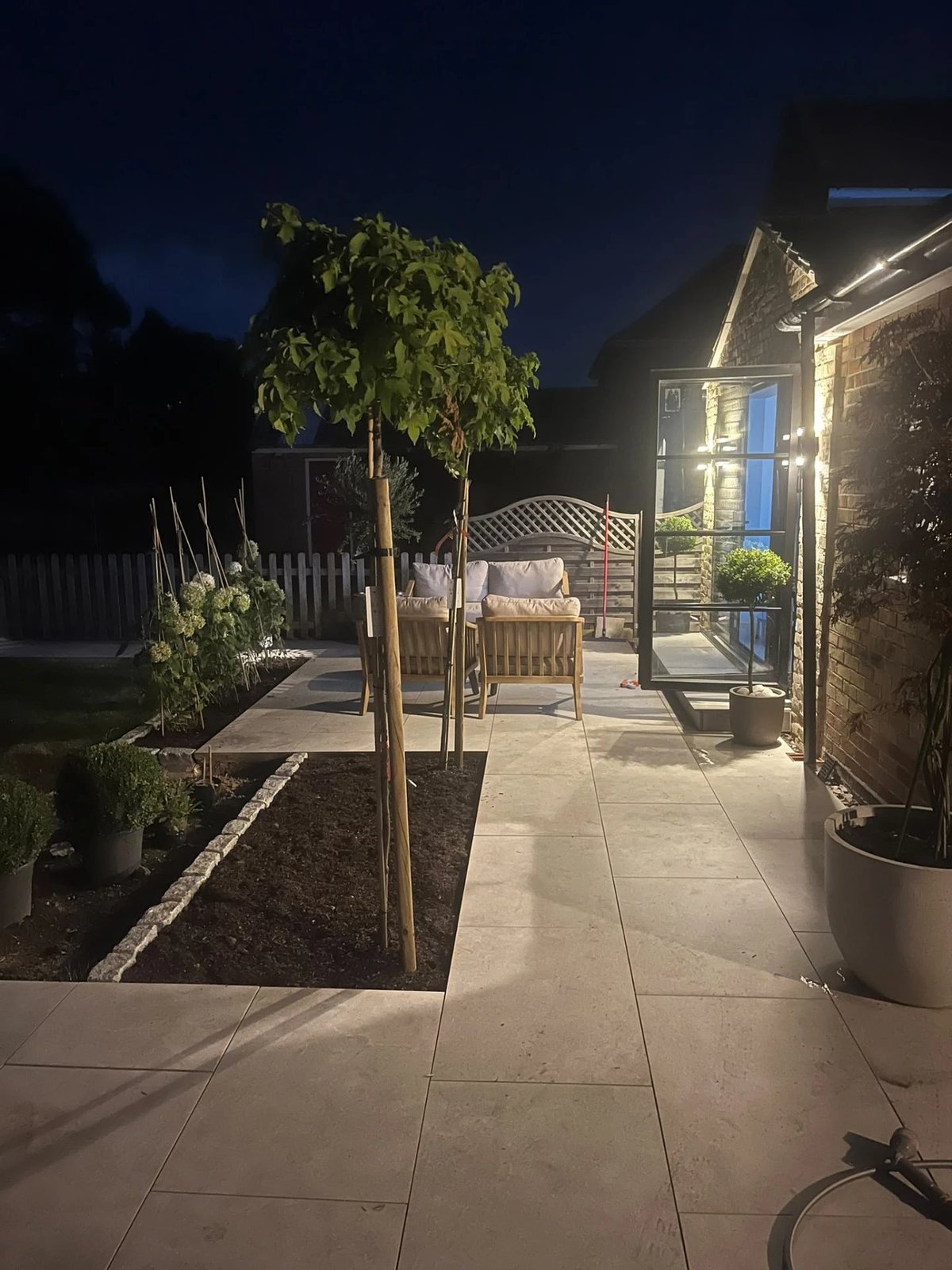 New porcelain patio and planting lit up at night outside the extension, Warboys