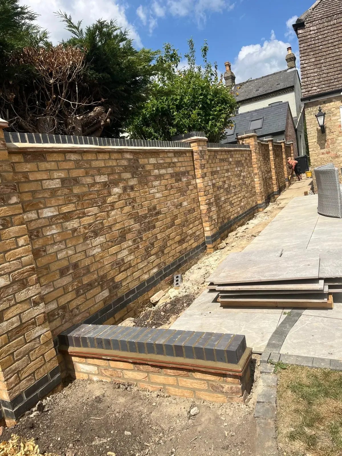 Long buff brick garden boundary wall with piers and dark brick detailing during construction