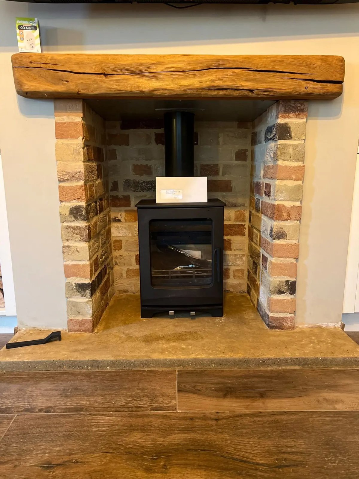 Log burner in a brick-lined fireplace with stone hearth and oak beam mantel, Warboys