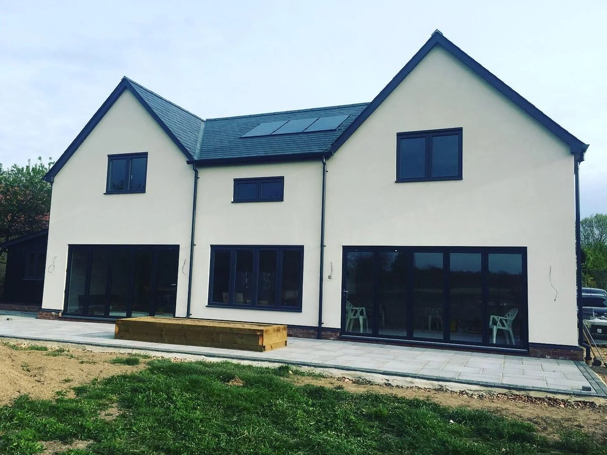 Completed rendered new-build home with dark windows, solar panels and rear patio
