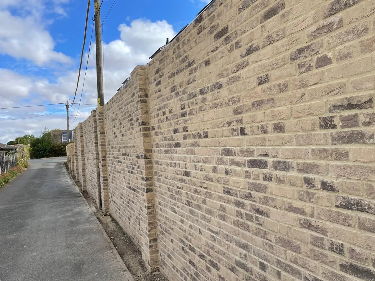 Completed long roadside buff brick boundary wall with regular supporting piers