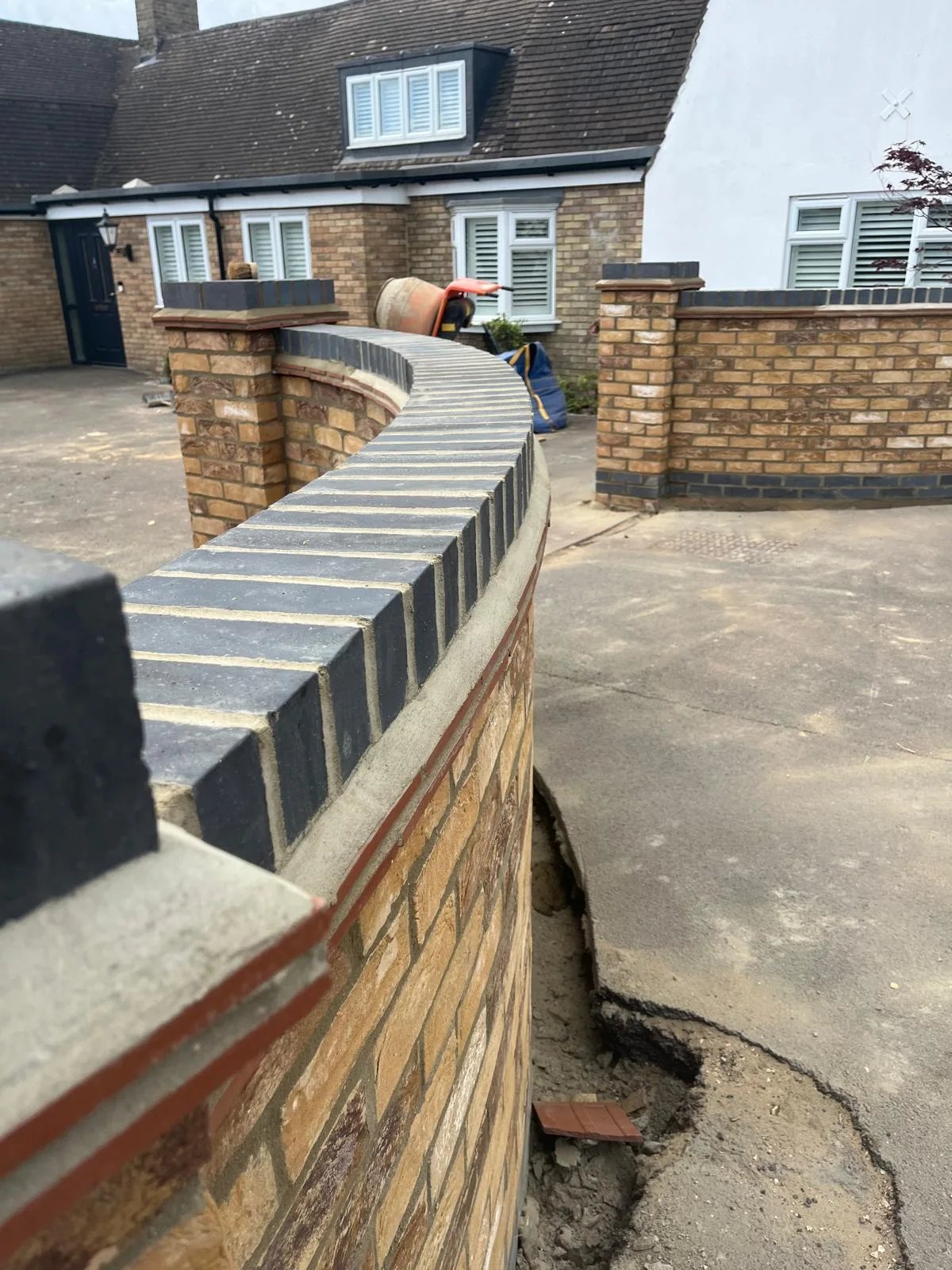 Curved buff brick entrance wall with contrasting dark brick coping during construction