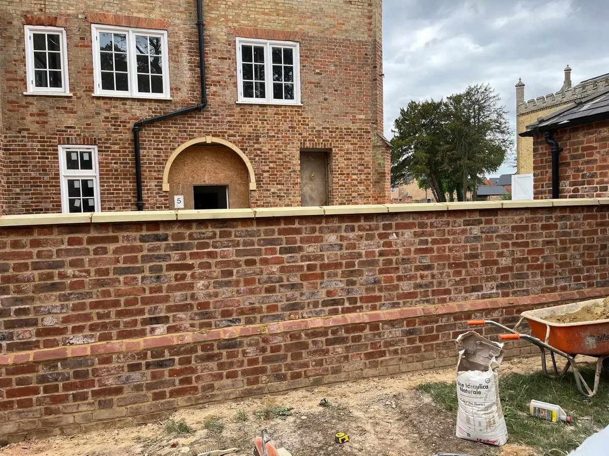 Traditional red brick boundary wall under construction beside a heritage property